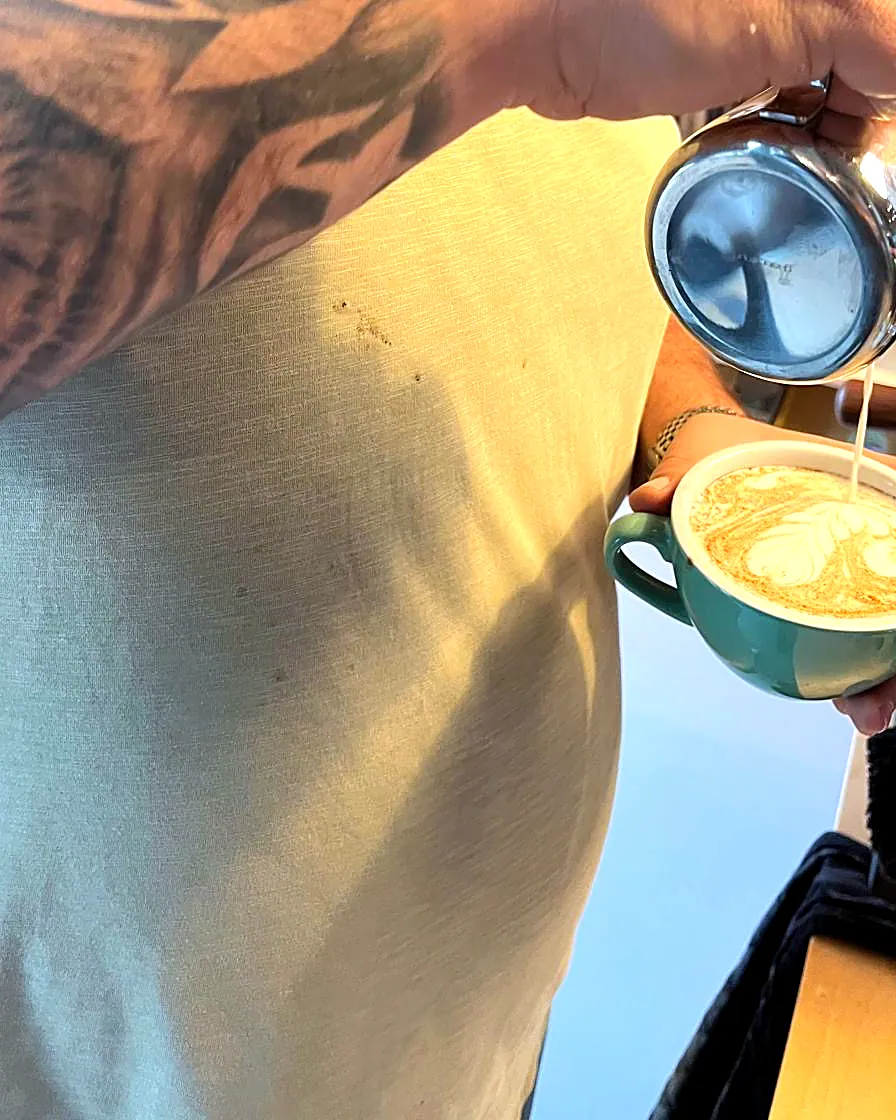 Hands pouring latte art from a steel jug