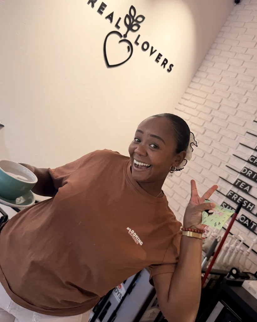 A barista with a cup under the Cereal Lovers logo, making a peace sign